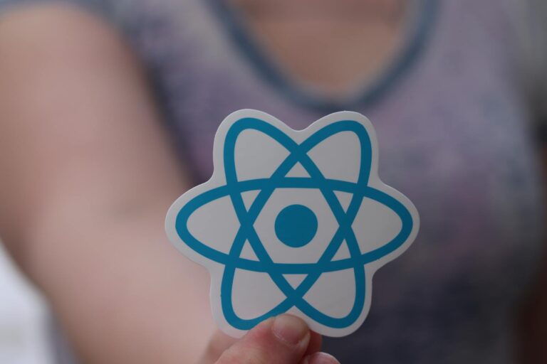 React Native 介紹 A person holds a sticker featuring the React logo, commonly used in web development.