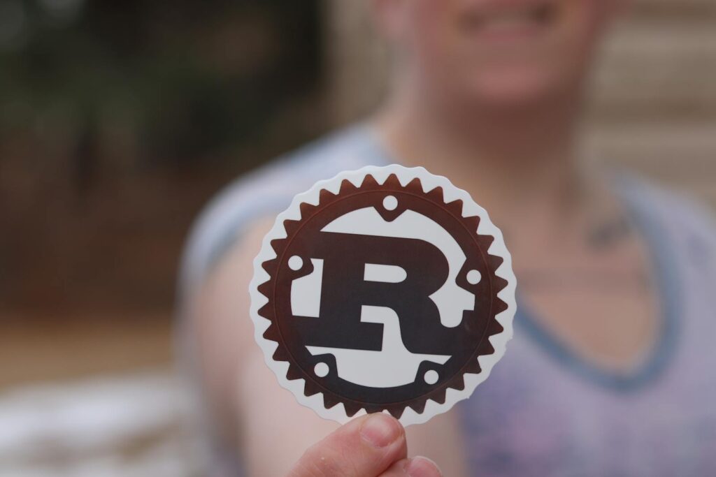 R 介紹 Person holding a Rust programming language logo sticker with blurred background.